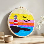Lighthouse at sunset over ocean punch needle artwork displayed on a table