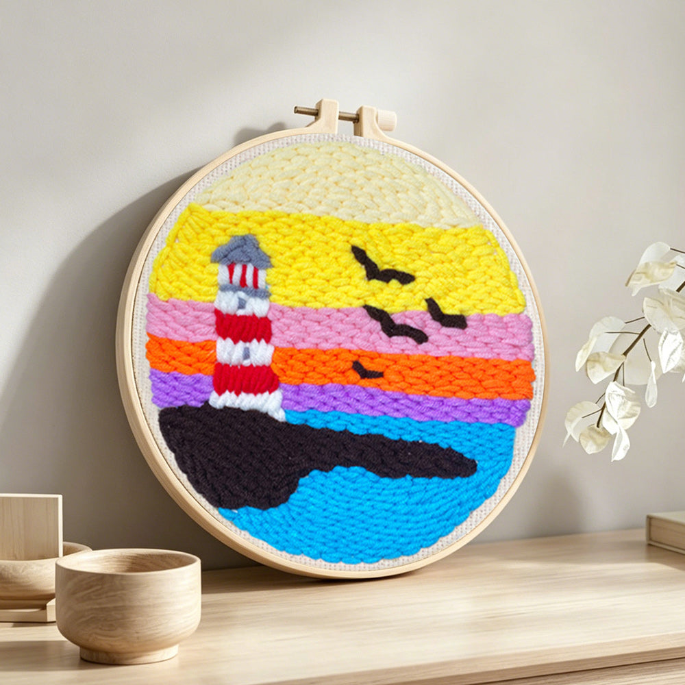 Lighthouse at sunset over ocean punch needle artwork displayed on a table