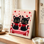 Matching black cats with red bows punch needle artwork displayed on a table