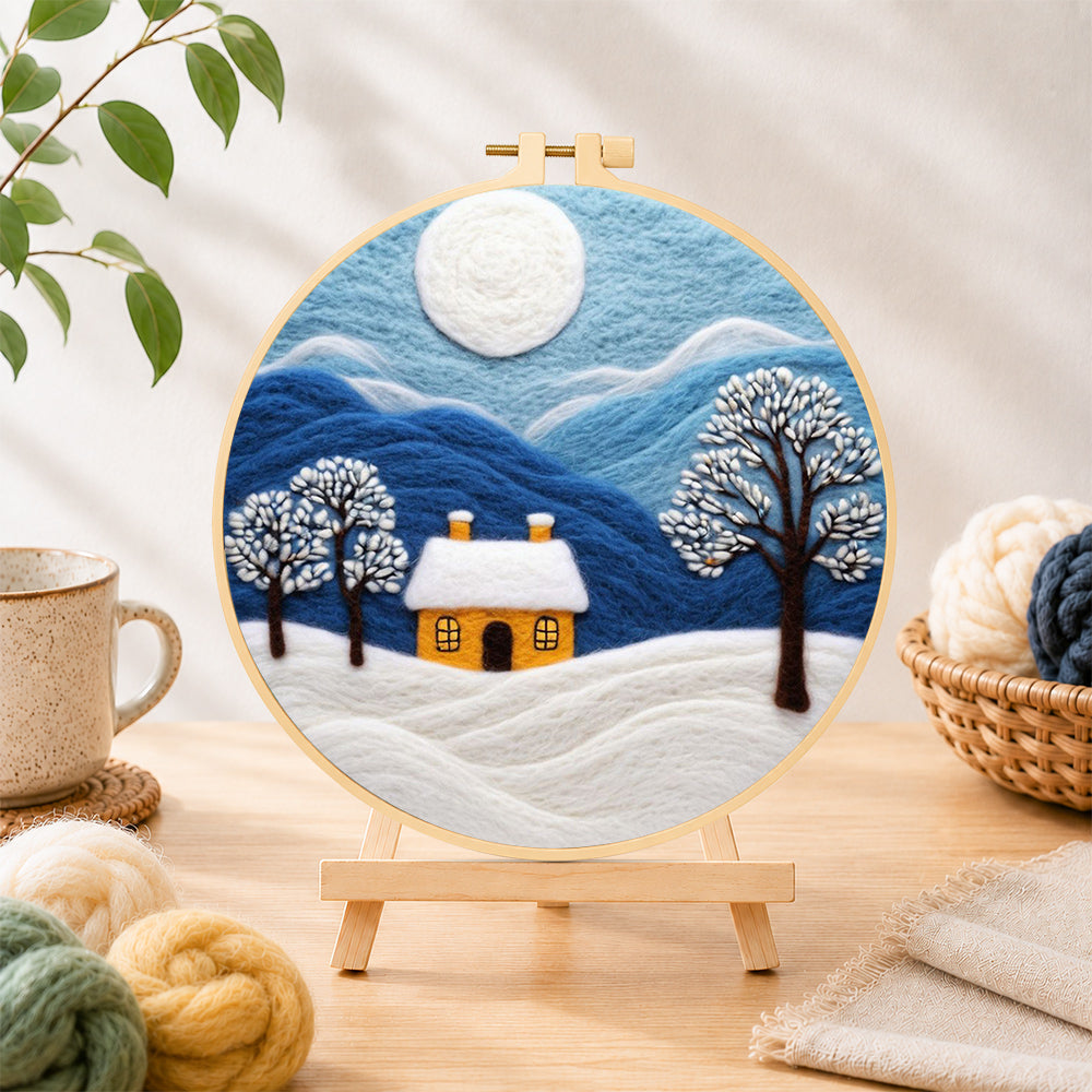 Finished minimalist blue mountains and snowy house needle felting displayed on a wooden easel
