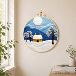Minimalist blue mountains and snowy house needle felt wall art displayed in a bright home interior