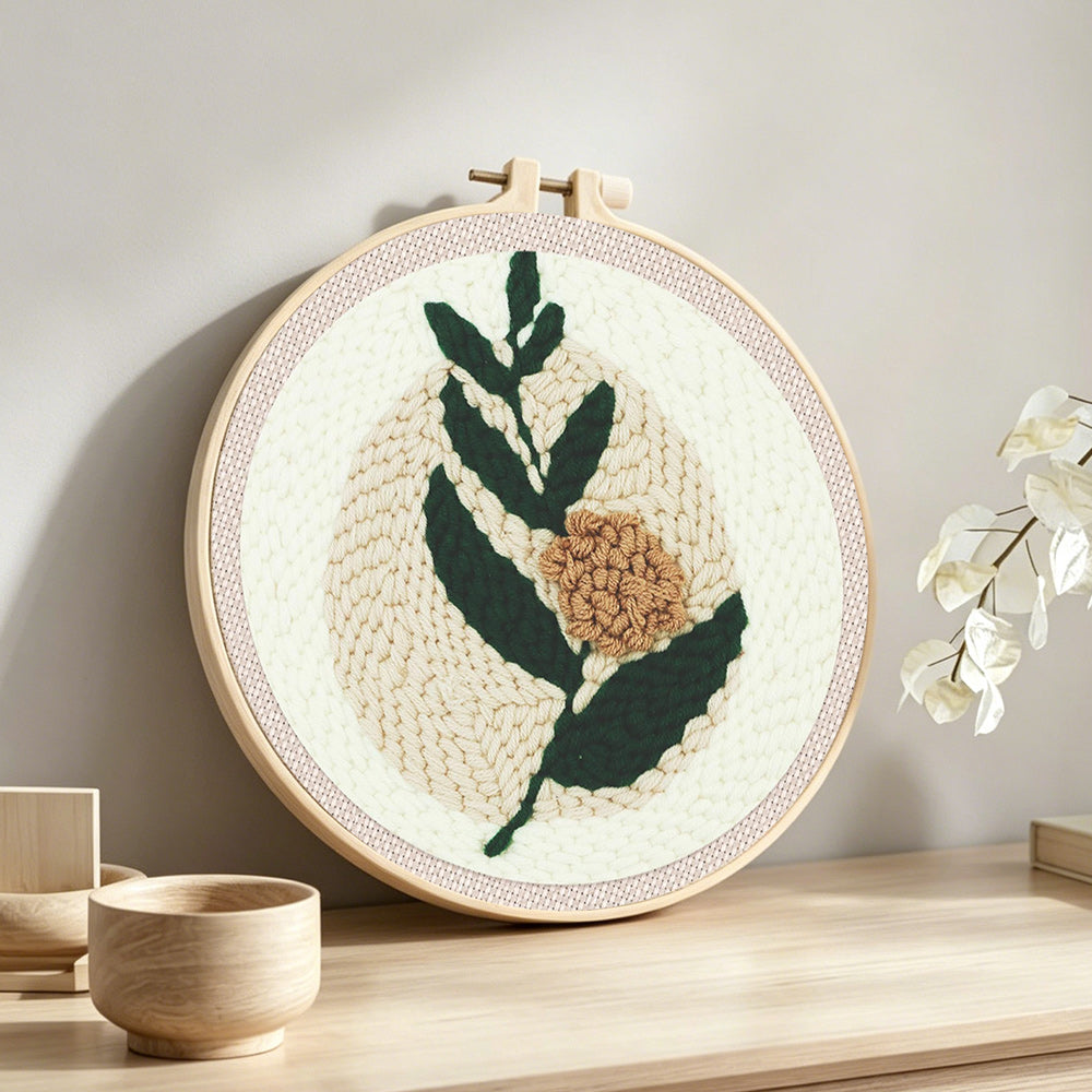 Minimalist green leaves and beige flower punch needle artwork displayed on a table