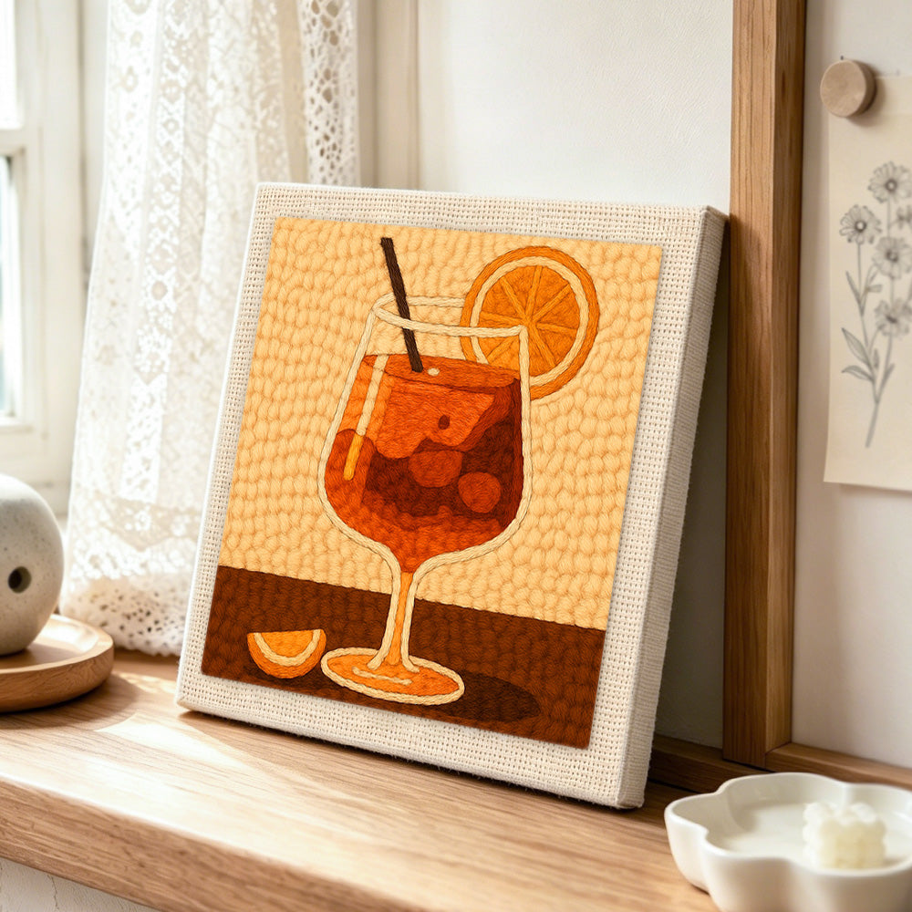 Minimalist orange cocktail with straw and citrus punch needle artwork displayed on a table