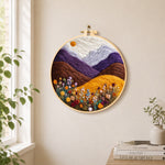 Misty purple mountains and wildflowers needle felt wall art displayed in a bright home interior