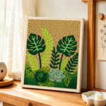 Monstera, ferns and succulents punch needle artwork displayed on a table