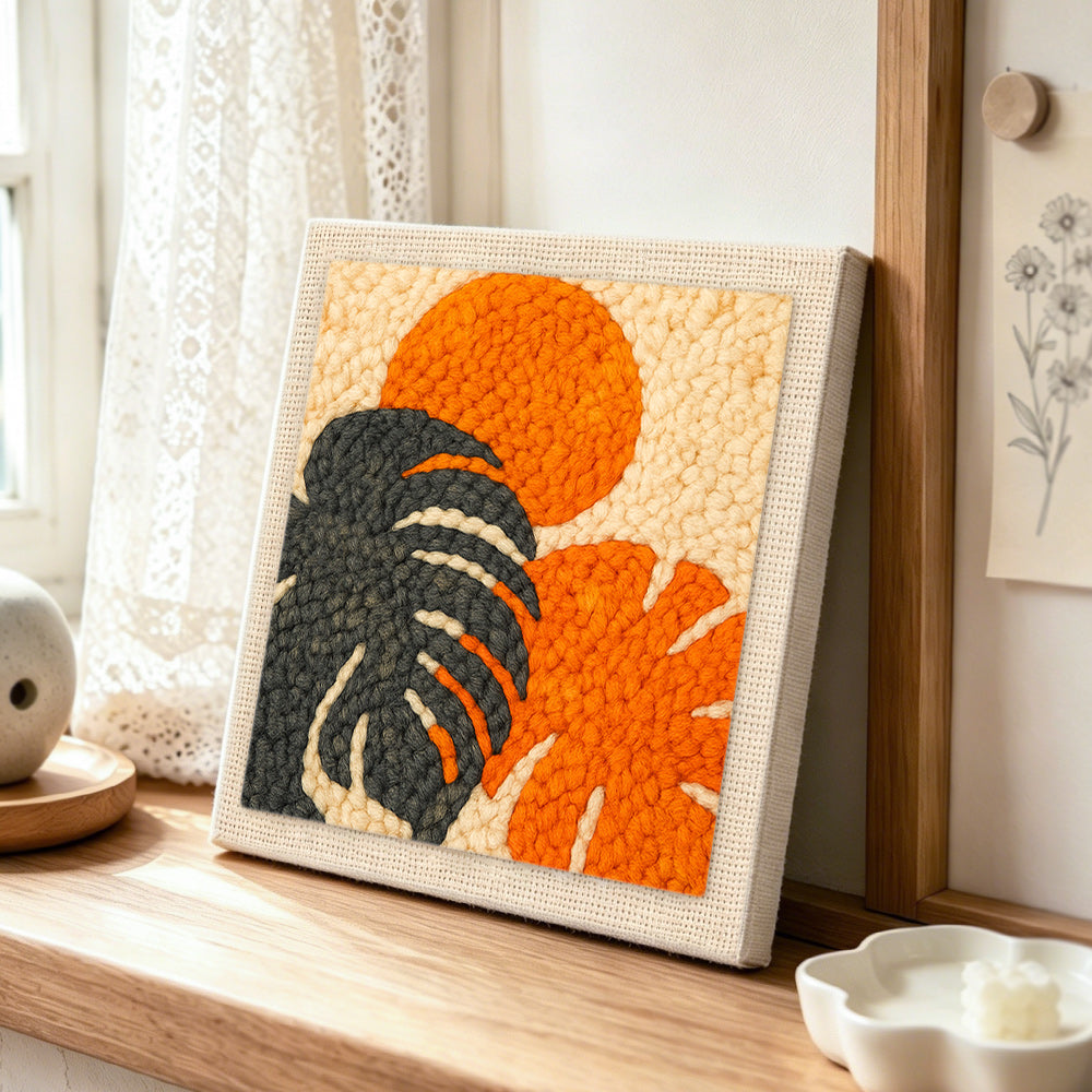 Monstera leaf and sun punch needle artwork displayed on a table