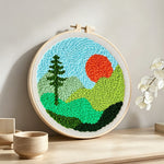 Mountain landscape with sun and tree punch needle artwork displayed on a table