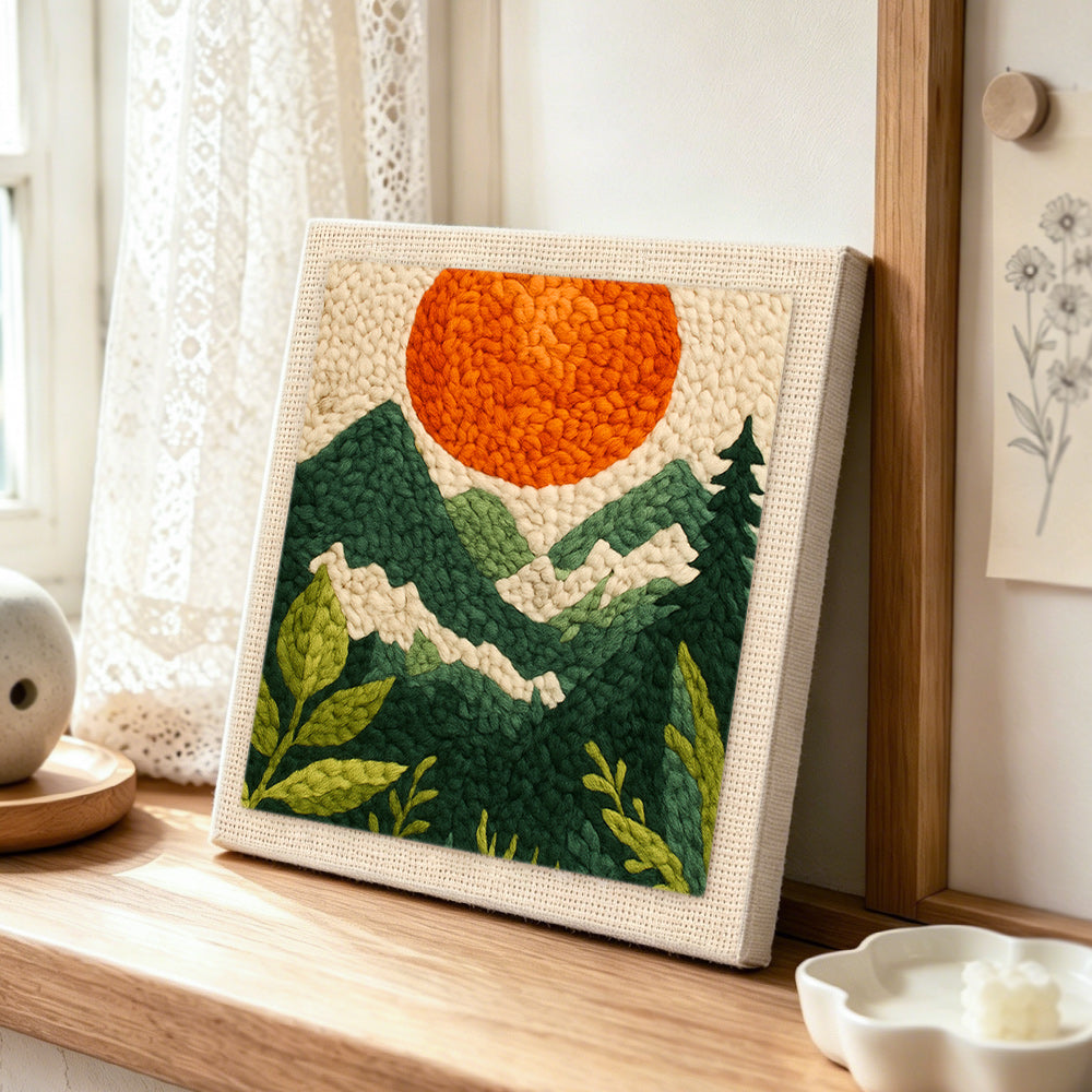 Mountain view and sunset punch needle artwork displayed on a table