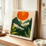 Mountain view and sunset punch needle artwork displayed on a table