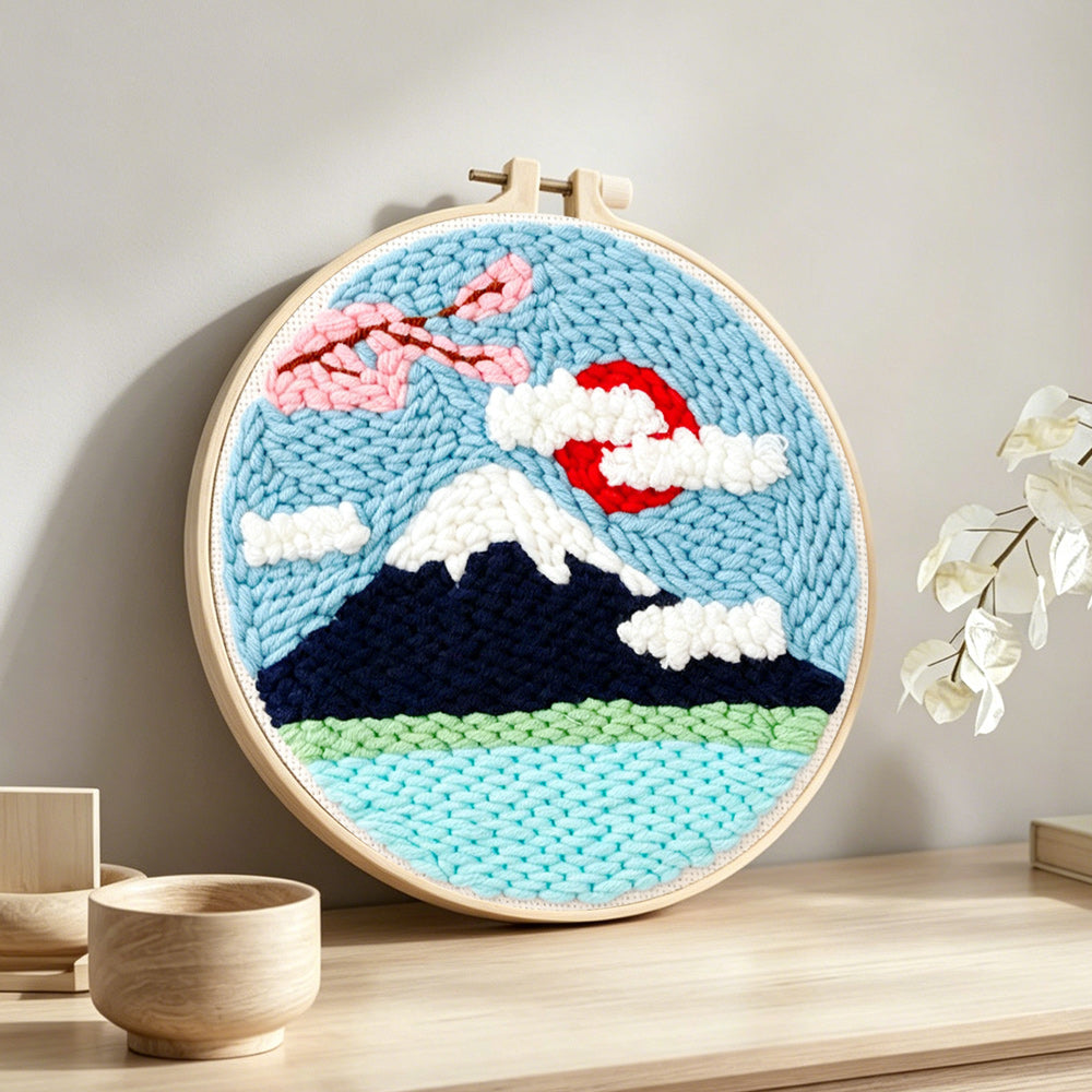 Mountain with snow and flowers punch needle artwork displayed on a table