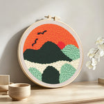 Mountains with flying birds at sunset punch needle artwork displayed on a table