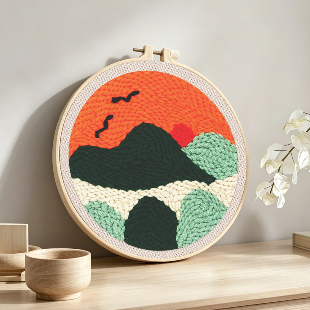 Mountains with flying birds at sunset punch needle artwork displayed on a table