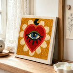 Mystical evil eye heart punch needle artwork displayed on a table