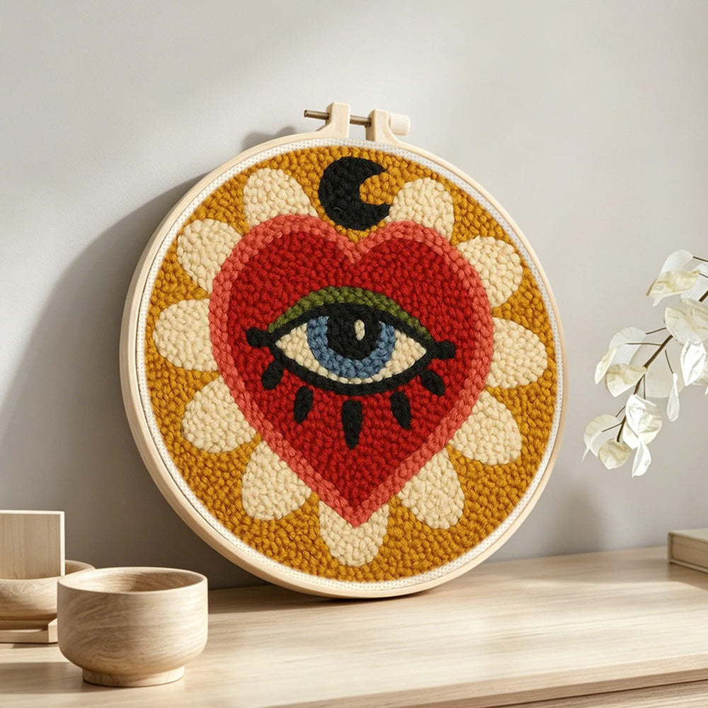 Mystical heart and evil eye sunburst punch needle artwork displayed on a table