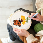 Creating handmade orange butterfly resting on flower punch needle artwork
