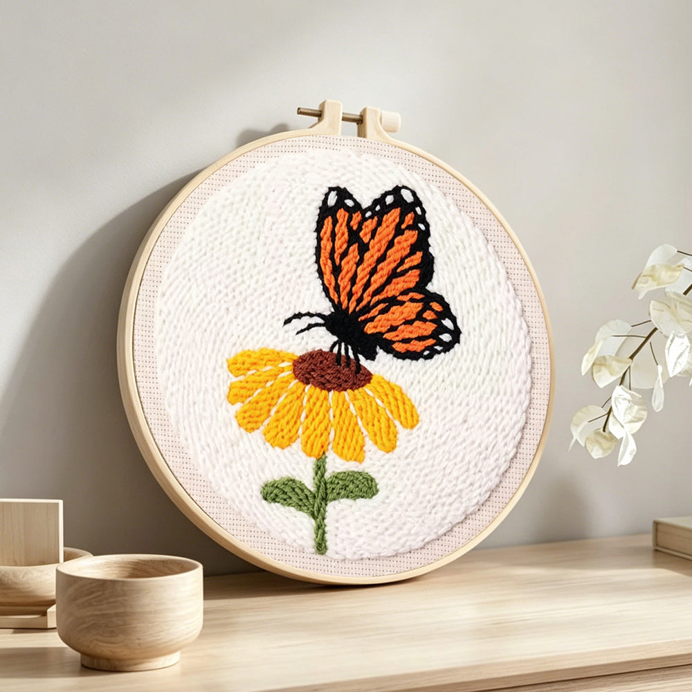 Orange butterfly resting on flower punch needle artwork displayed on a table