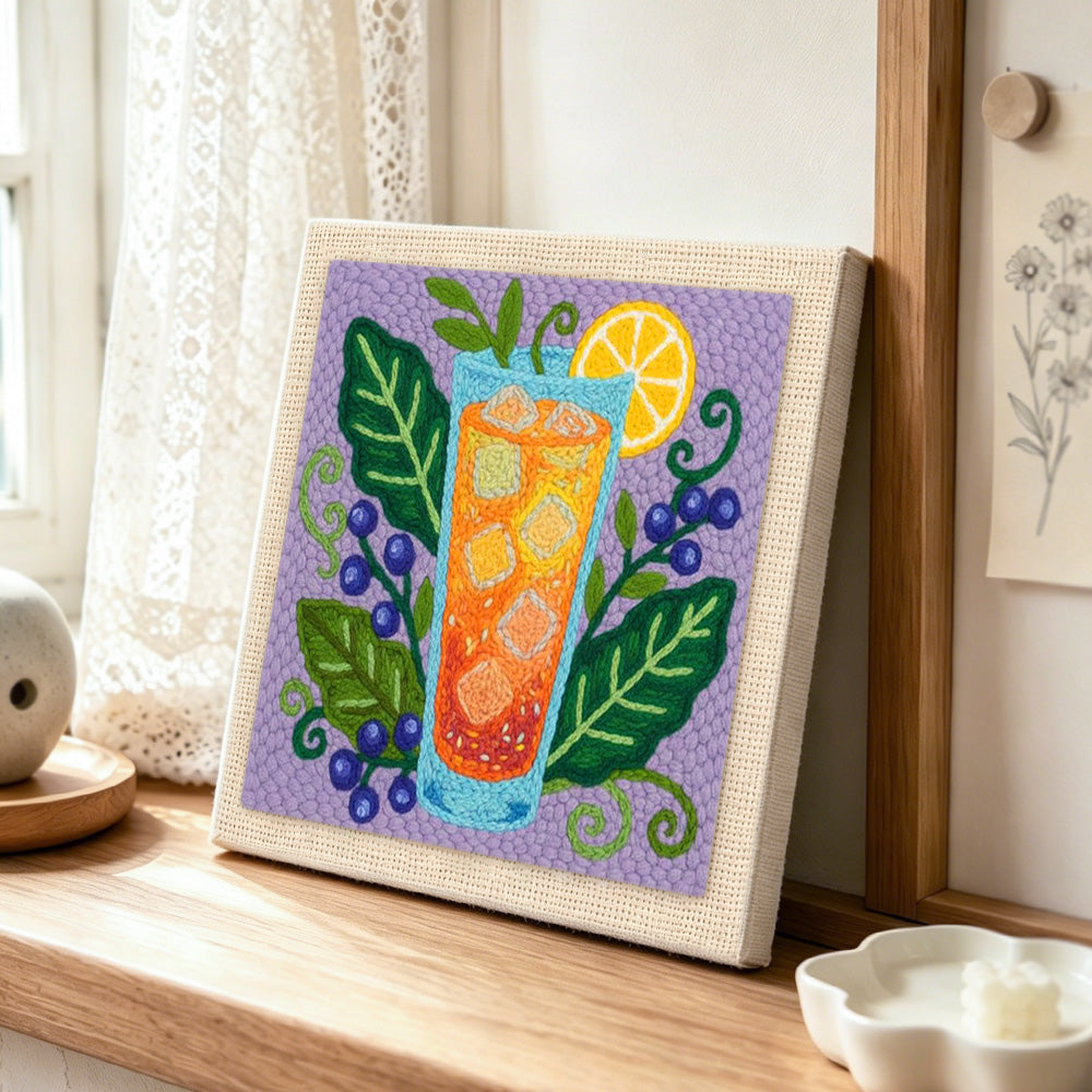 Orange cocktail, blueberries and botanical leaves punch needle artwork displayed on a table