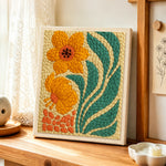 Orange flowers with giant leaves punch needle artwork displayed on a table