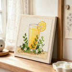 Orange juice and green leaves punch needle artwork displayed on a table