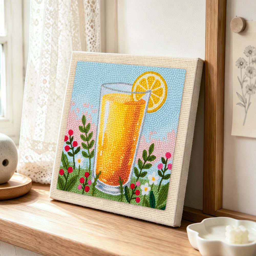 Orange juice and some wildflowers punch needle artwork displayed on a table
