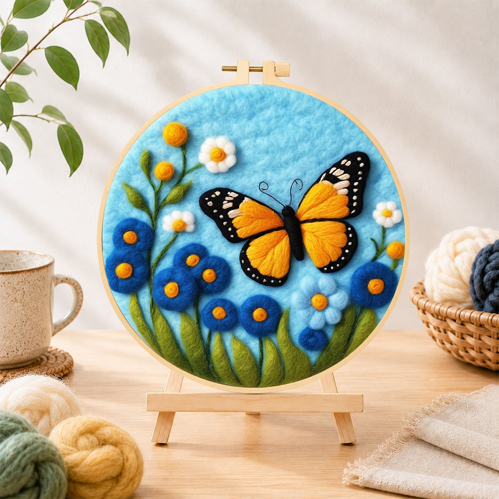Finished orange monarch butterfly and blue flowers needle felting displayed on a wooden easel