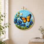 Orange monarch butterfly and blue flowers needle felt wall art displayed in a bright home interior