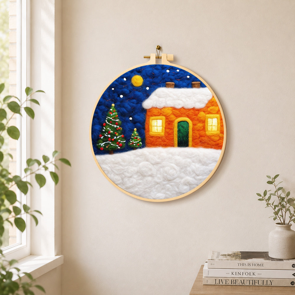 Orange snowy house and christmas trees needle felt wall art displayed in a bright home interior