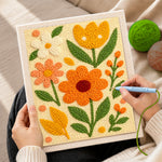 Creating handmade orange, yellow and white blooms with green leaves punch needle artwork