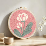 Pale pink background with white flowers punch needle artwork displayed on a table