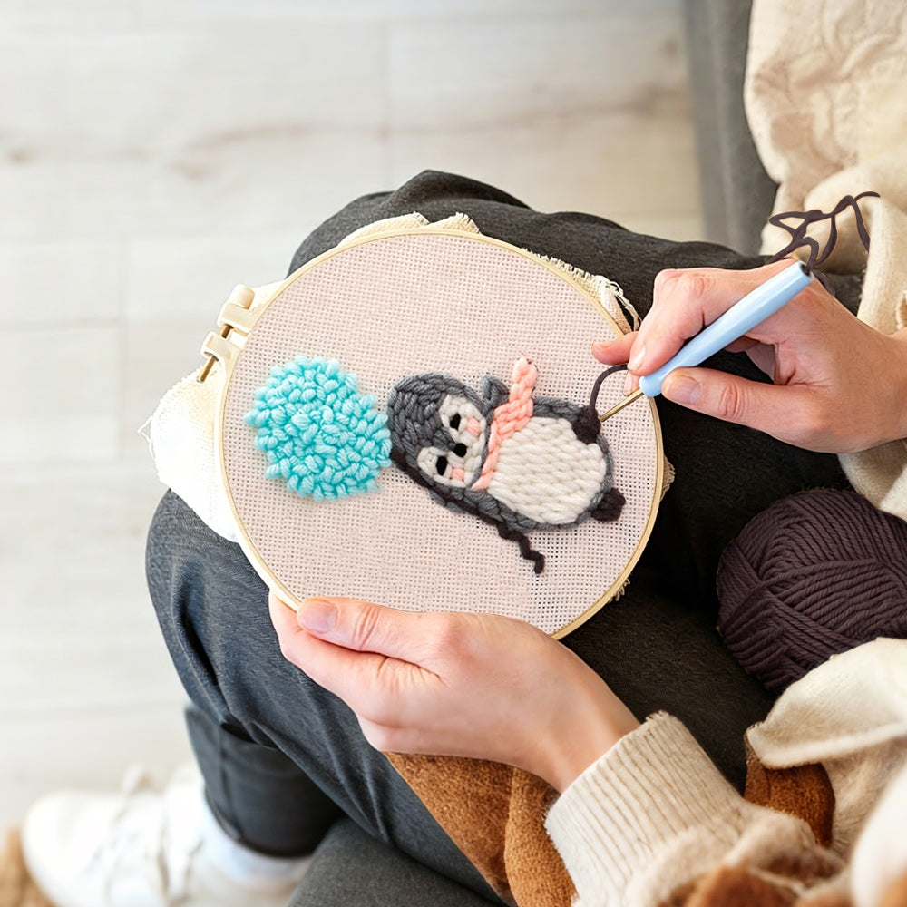 Creating handmade penguin with blue balloon pom punch needle artwork