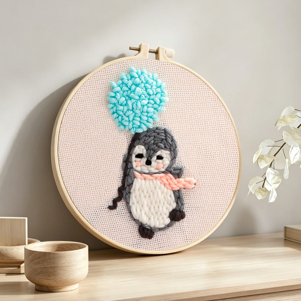 Penguin with blue balloon pom punch needle artwork displayed on a table