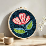 Pink and white flower on navy blue punch needle artwork displayed on a table