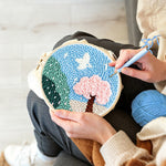 Creating handmade pink blossom tree and green mountains punch needle artwork