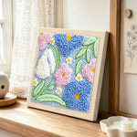 Pink, blue and white blossoms punch needle artwork displayed on a table