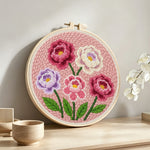 Pink, purple and white layered flowers punch needle artwork displayed on a table