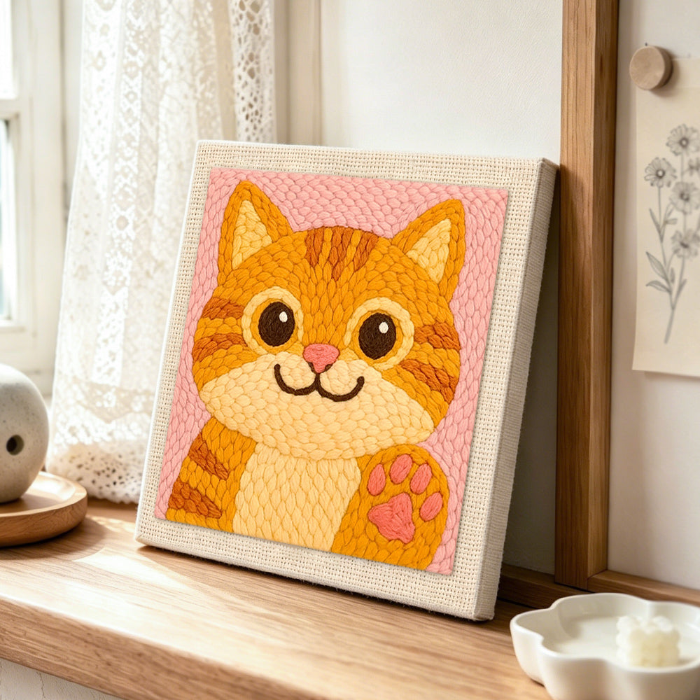 Playful orange cat waving paw punch needle artwork displayed on a table