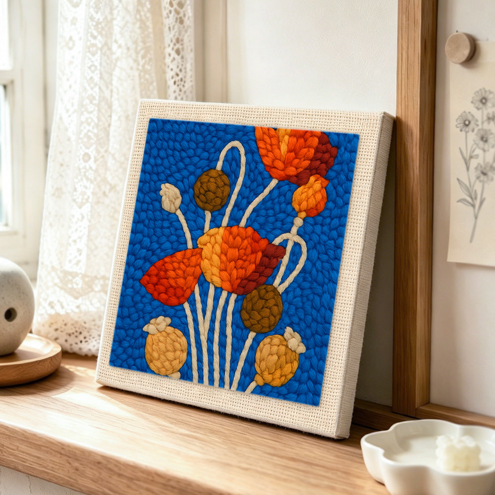 Poppy flowers and seeds punch needle artwork displayed on a table