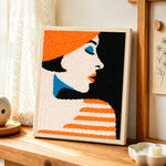 Profile of woman in orange hat punch needle artwork displayed on a table