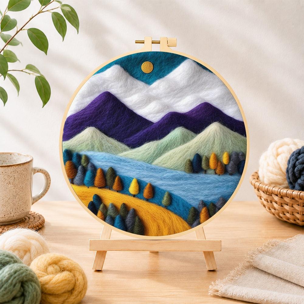 Finished purple and white mountains with vibrant trees needle felting displayed on a wooden easel