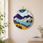 Purple and white mountains with vibrant trees needle felt wall art displayed in a bright home interior