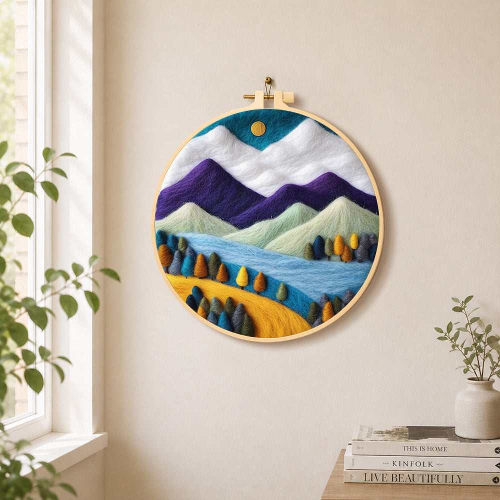 Purple and white mountains with vibrant trees needle felt wall art displayed in a bright home interior