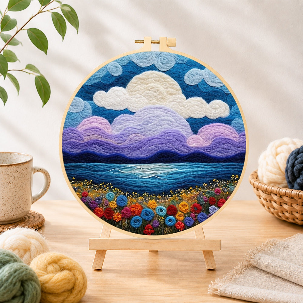 Finished purple clouds and flower-covered coastline needle felting displayed on a wooden easel