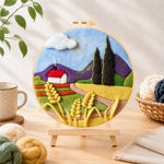 Finished purple mountains and wheat cottage needle felting displayed on a wooden easel