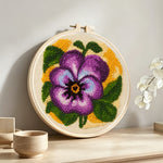 Purple pansy flower punch needle artwork displayed on a table