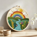 Rainbow over the rolling river and green fields punch needle artwork displayed on a table
