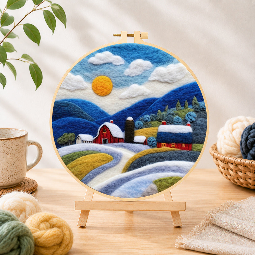 Finished red barn and snowy blue hills needle felting displayed on a wooden easel