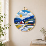 Red barn and snowy blue hills needle felt wall art displayed in a bright home interior