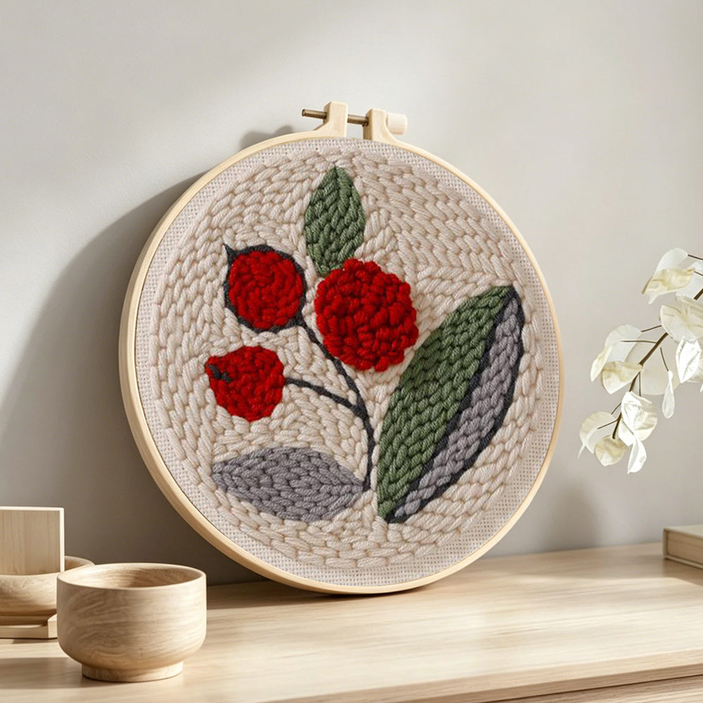 Red berries with green leaves punch needle artwork displayed on a table