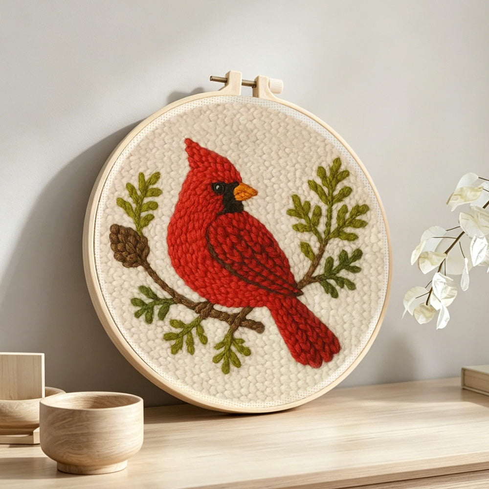 Red cardinal and pine cone branch punch needle artwork displayed on a table