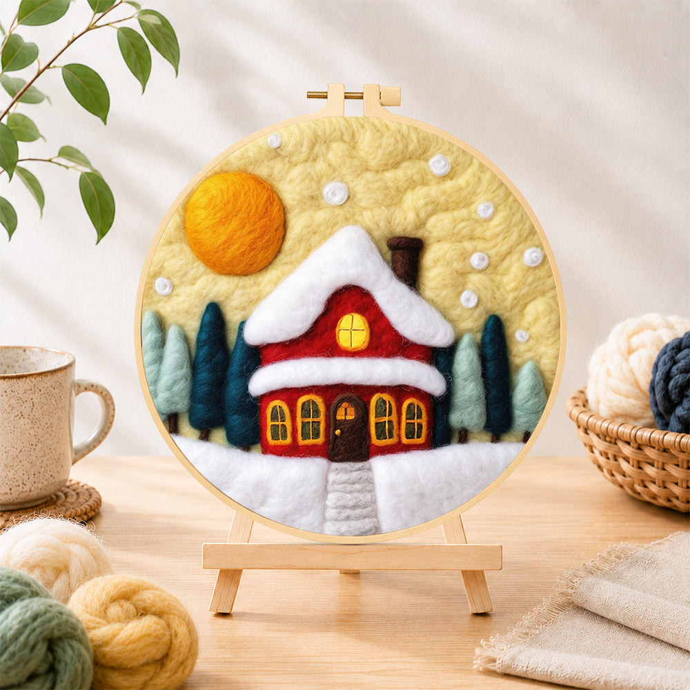 Finished red cottage under snowy yellow sky needle felting displayed on a wooden easel